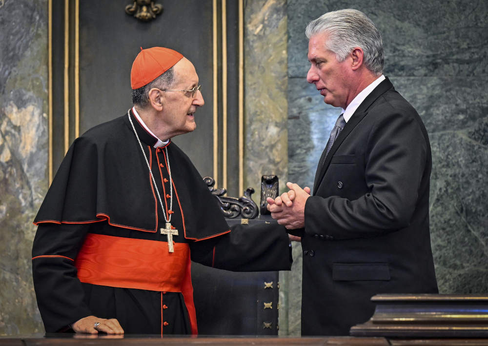 A white cardinal shakes hands with a white man in a suit