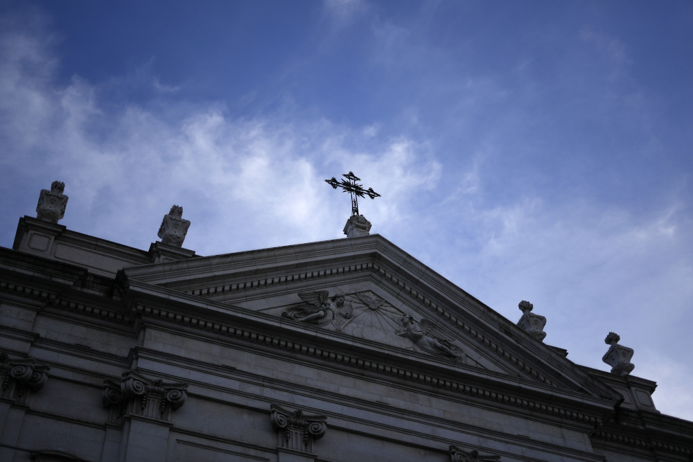 A view of the shadowed upper half of a stone church topped by a cross and the sky