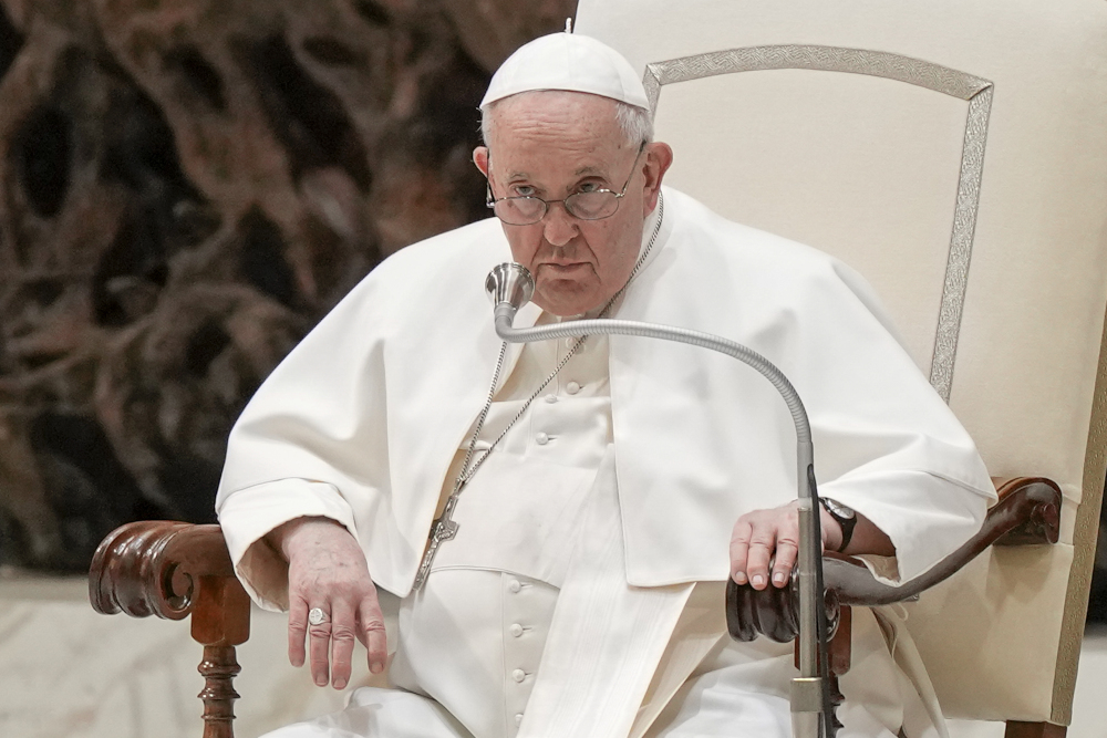 Pope Francis looks serious in his white chair with a microphone in front of his face