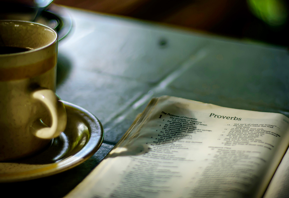 The Bible open to the Book of Proverbs, sitting next to a coffee cup (Unsplash/Alex Shute)