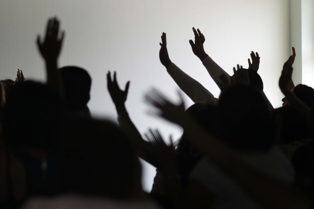 The silhouettes of people with their hands raised in the air in a praise and worship posture