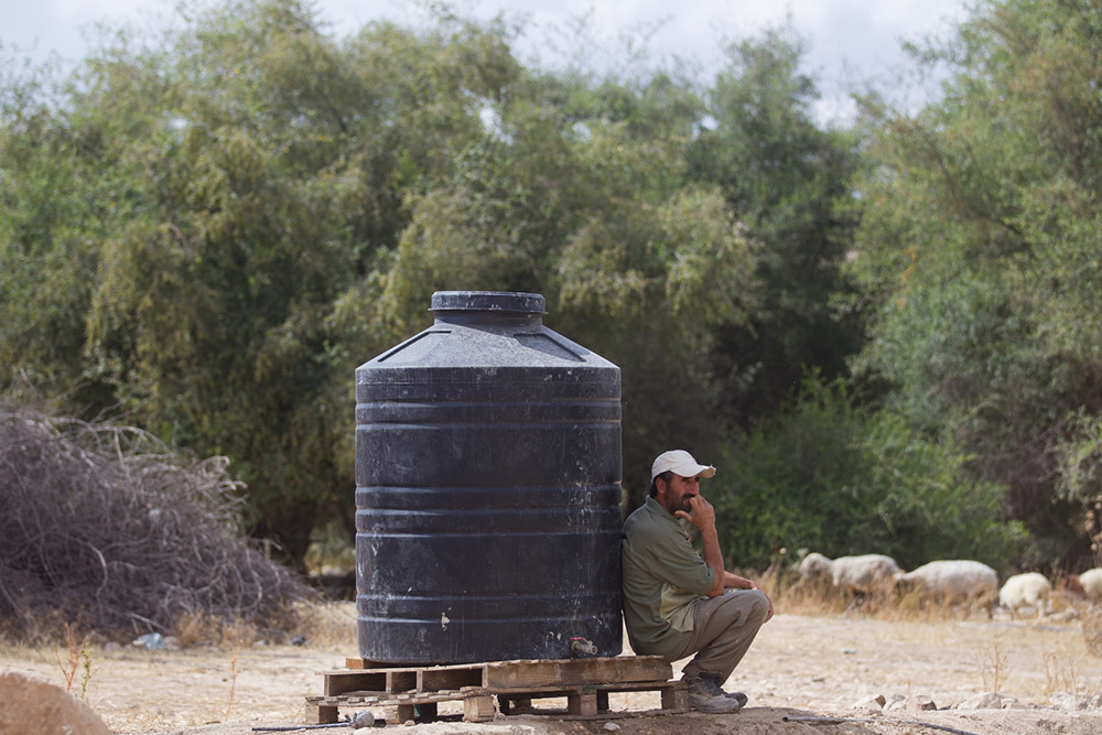 A Palestinian man leans up against a water tank in Fasayel, West Bank. (CNS/Miriam Alster)