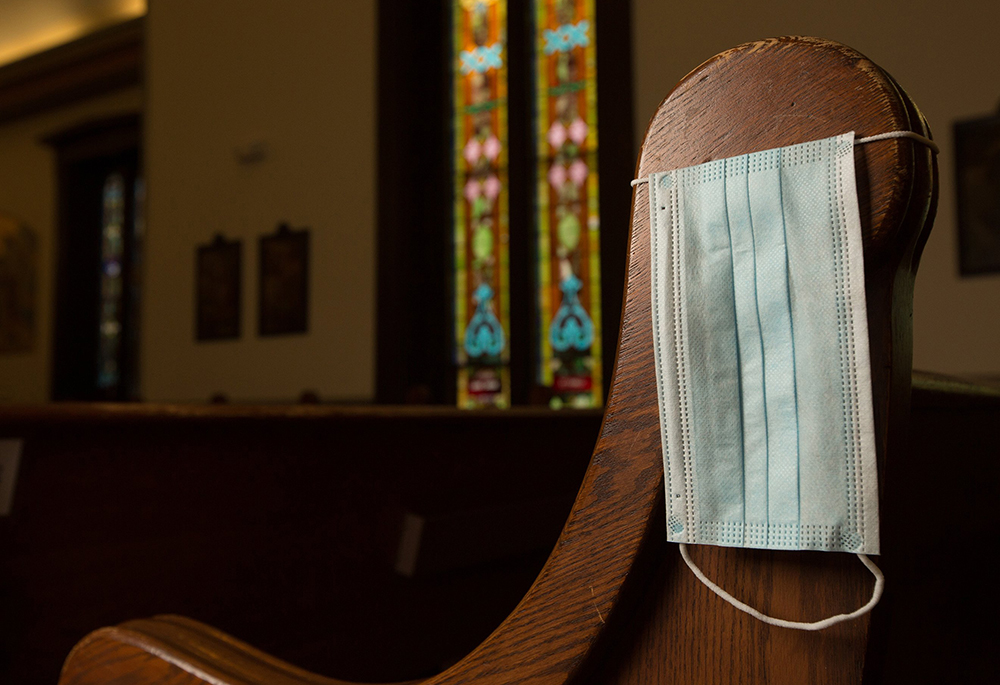 In this illustration photo, a disposable medical mask hangs on the side of a pew. (CNS/The Catholic Spirit/Dave Hrbacek)