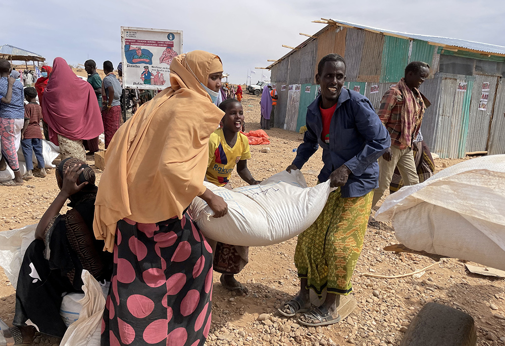 People receive bags of relief grains at a camp for the internally displaced people Jan. 22, 2022, in Adadle, Ethiopia. The war in Ukraine, ongoing instability in Tigray and global inflation — peaking at 43% for food items in Ethiopia in April 2022 — placed additional burdens on humanitarian and pastoral efforts in Ethiopia. (CNS/Claire Nevill, World Food Program handout via Reuters)