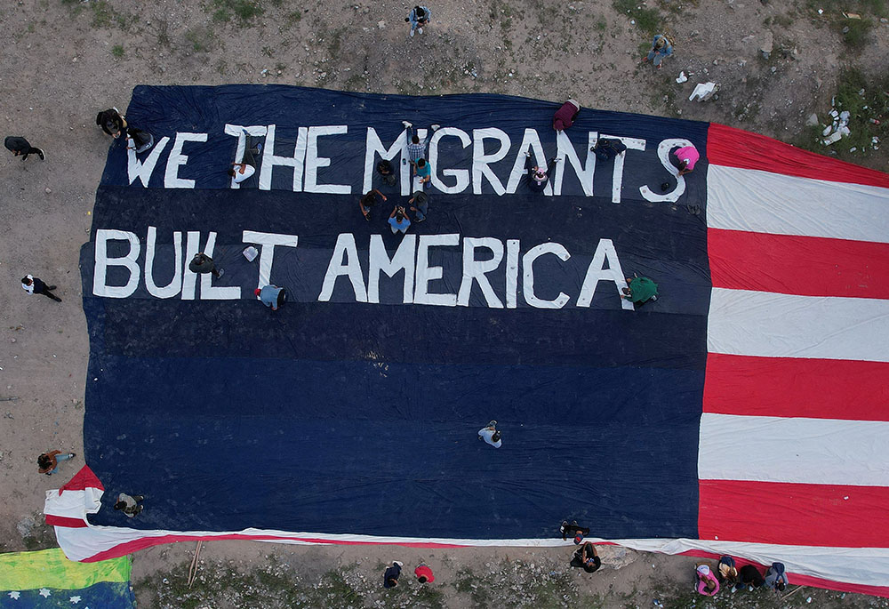 Migrants at a camp near the banks of the Rio Bravo in Ciudad Juárez, Mexico, make a large banner in the likeness of the U.S. flag Oct. 30, 2022. (CNS/Reuters/Jose Luis Gonzalez)