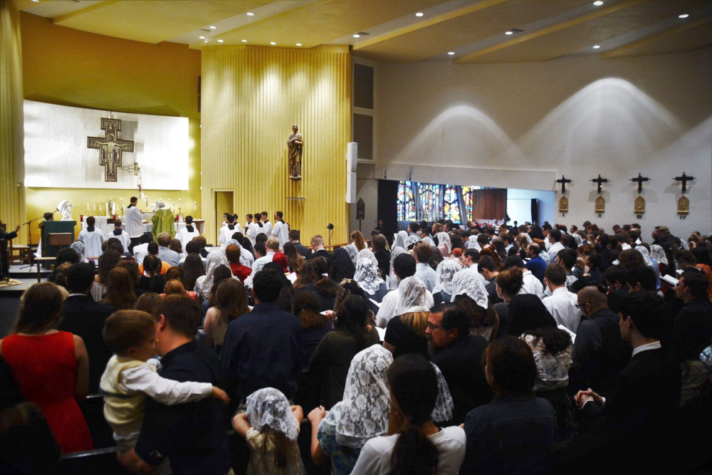 A photo from the back of a group of people gathered for mass. Women have lace headcoverings, and all altar servers are male.