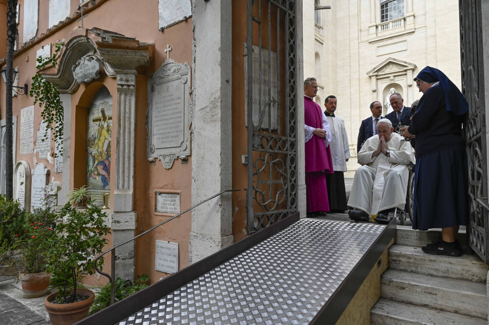 Pope Francis prays, sitting in a wheelchair at the top of a ramp