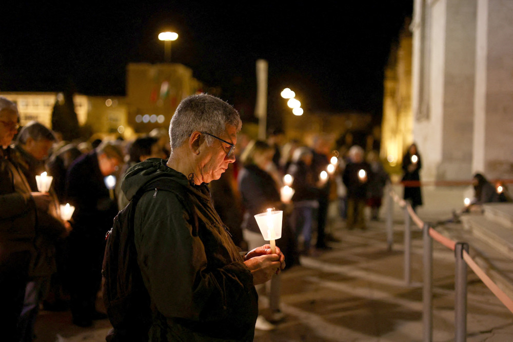 An older white man holds a candle while standing outside in a crowd at night