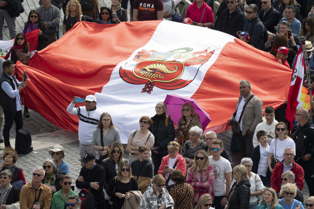 A crowd stands in St. Peter's Square, with a group holding a very large red and white Peruvian flag