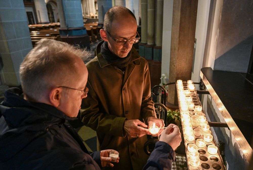 Two men light votive candles in a church.