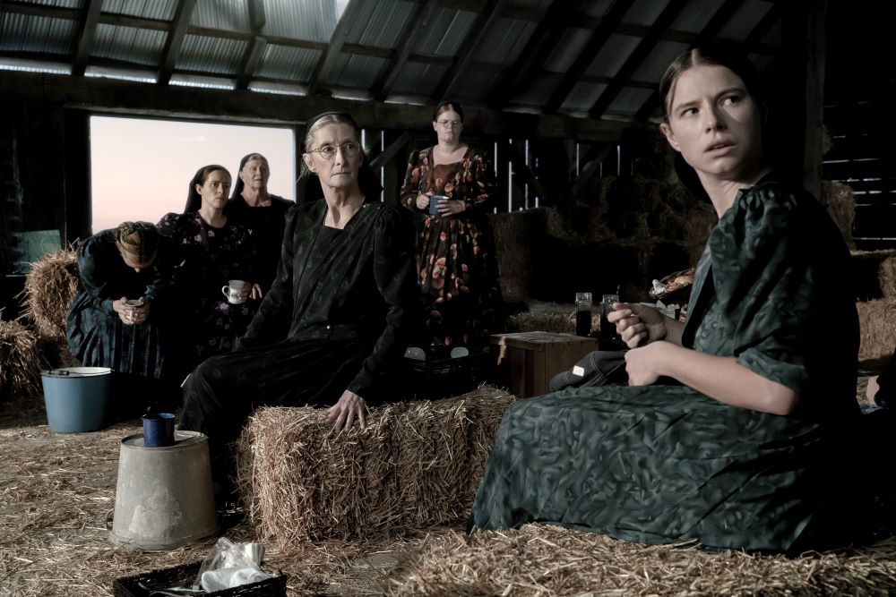 A still shot of the movie "Women Talking" shows women sitting in a barn.