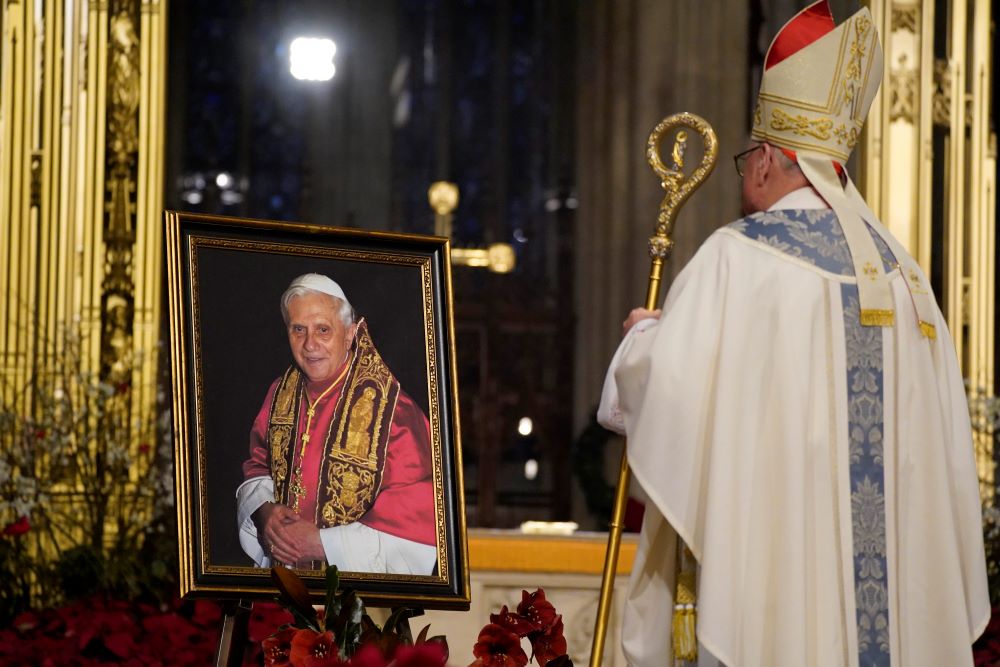 New York Cardinal Dolan, with his back to camera, views a portrait of Pope Benedict XVI. 