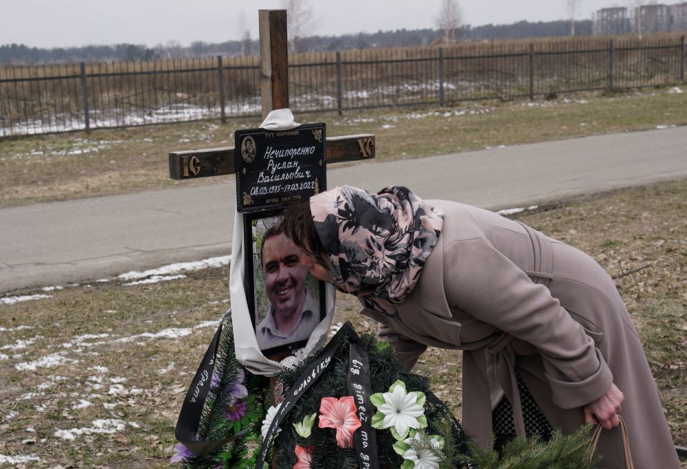 A Ukrainian woman kisses cross atop husband's grave. 