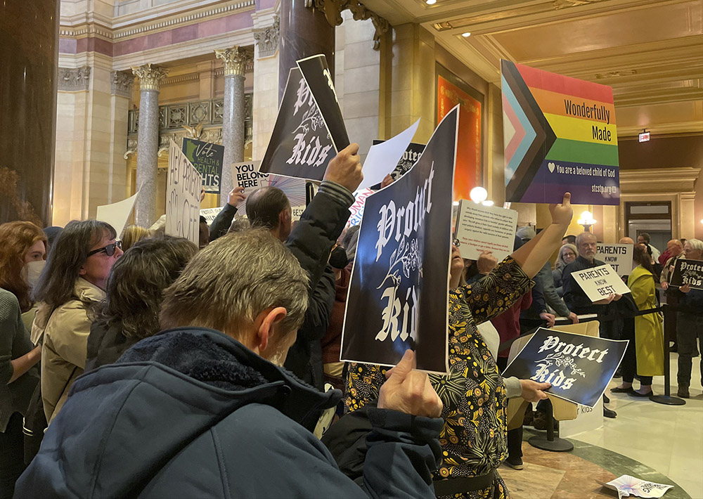 Protesters hold signs as they chant for and against a bill that would make Minnesota a trans refuge state, and strengthen protections for kids and their families who come to the state for gender-affirming care, outside the room where lawmakers would vote on the bill at the state capitol March 23 in St. Paul. The Minnesota House passed the bill early the next morning. (AP/Trisha Ahmed)