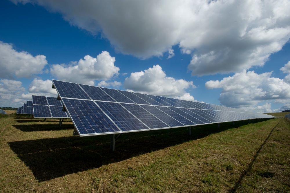 solar panels in a field with blue sky and clouds overhead 