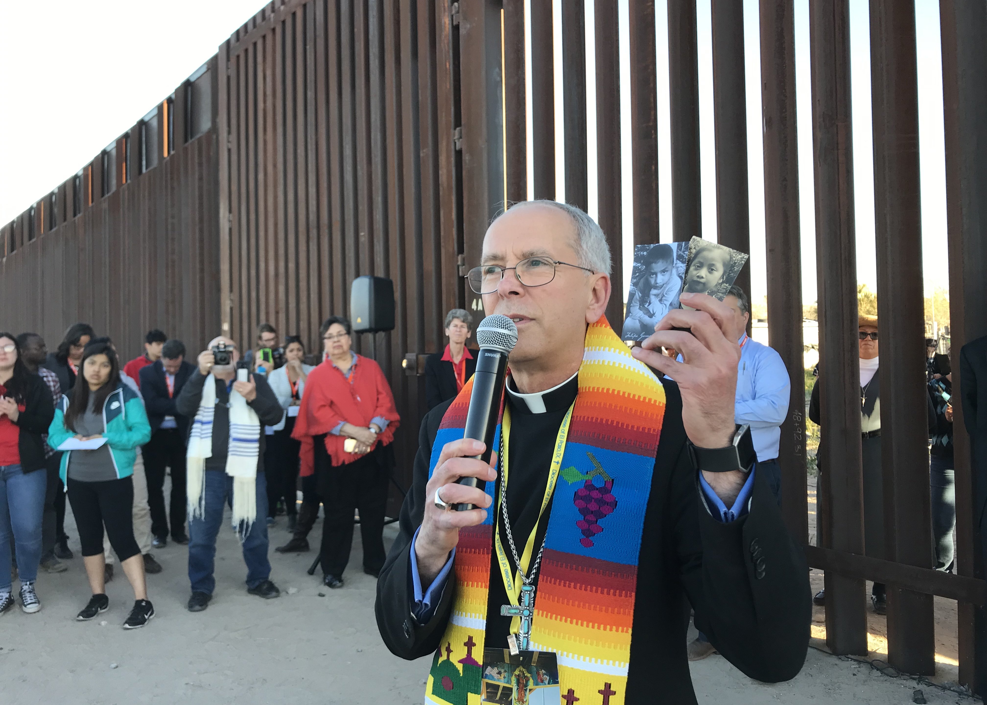 Bishop Mark Seitz of El Paso, Texas, is seen Feb. 26, 2019, at the U.S.-Mexico border wall holding photos of two migrant children who died in U.S. custody. (CNS/David Agren)