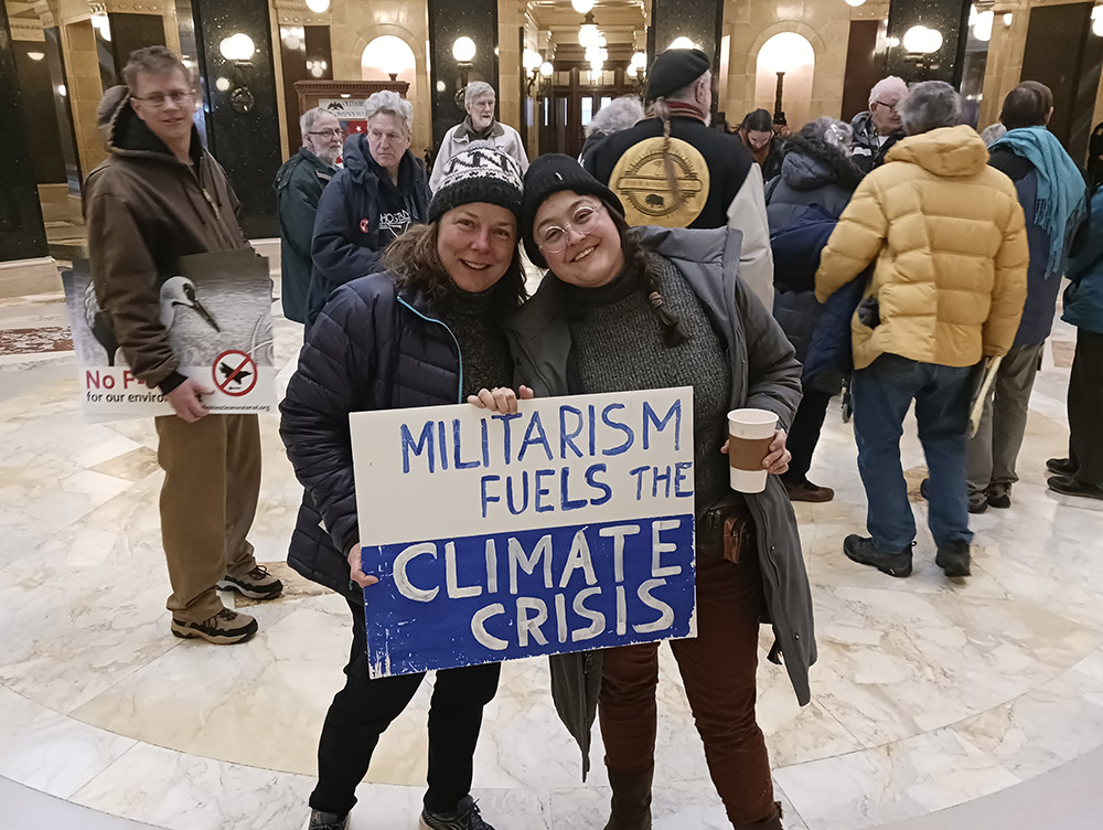 Chrissy Kirchhoefer, left, and Lindsey Myers, St. Louis-area Catholic Workers, hold a sign during a witness in the Wisconsin State Capitol in Madison on March 27. (NCR photo/Theodore Kayser)