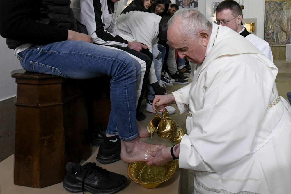 Pope Francis, without his zuchetto, pours water over a person's foot, who can be seen from the waist down wearing jeans