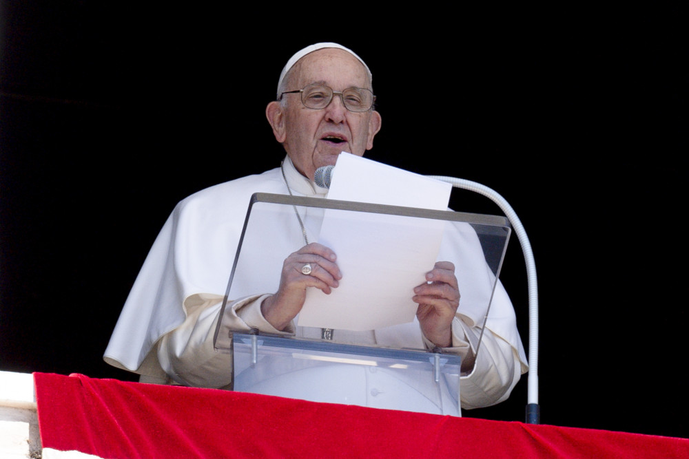 Pope Francis reads from a sheet of paper, while standing behind a microphone and a clear lecturn