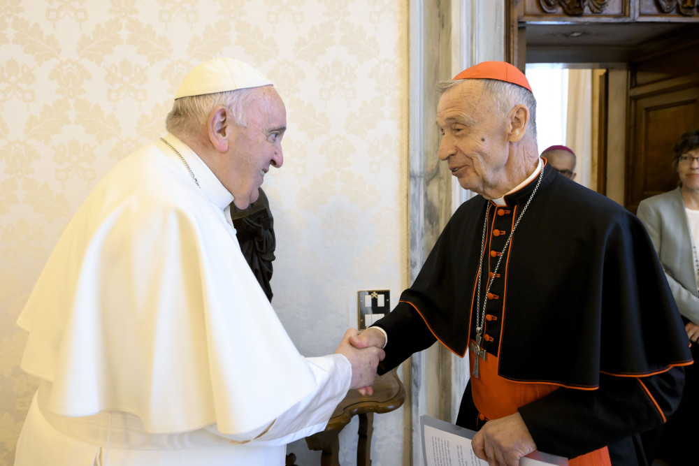 Pope Francis shakes an older white cardinal's hand