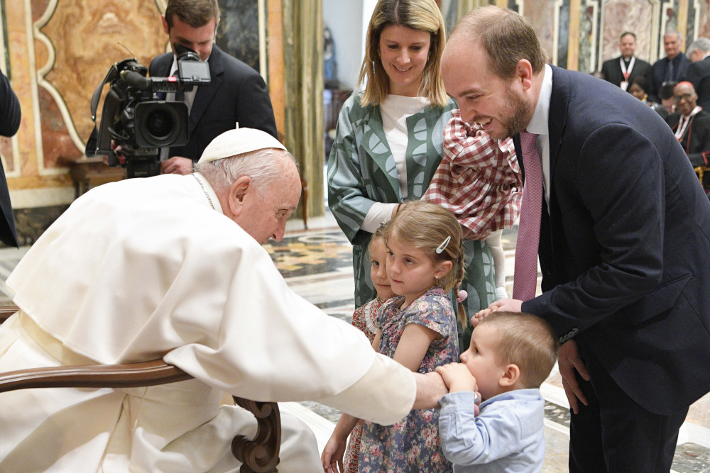 A toddler holds Pope Francis' hand as his sisters and parents stand around him