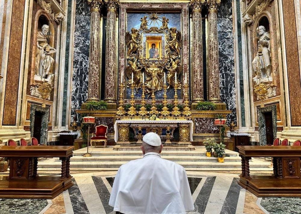 Pope Francis is shown from the back as he prays to icon of Mary.