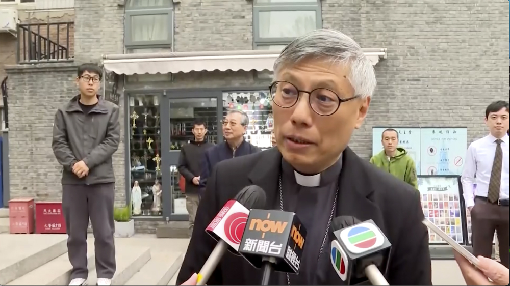 In this image from a video shot by Hong Kong broadcaster TVB, Hong Kong Bishop Stephen Chow talks to media during his visit to Beijing, with unidentified men standing behind him, on Thursday, April 20, 2023. (TVB via AP)