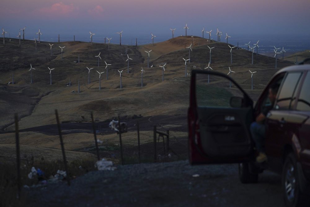 A man looks out at wind turbines in Livermore, Calif., Wednesday, Aug. 10, 2022. (AP/Godofredo A. Vásquez)