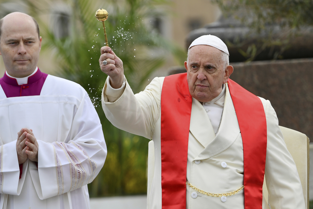 Dressed in a white coat and a red stole, Pope Francis holds aloft a holy water sprinkler