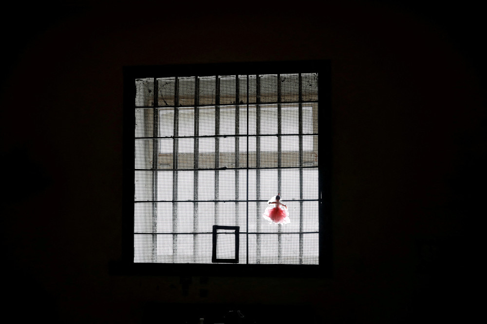A lit window in the dark is covered by mesh and metal bars with a pink rag doll hanging from it