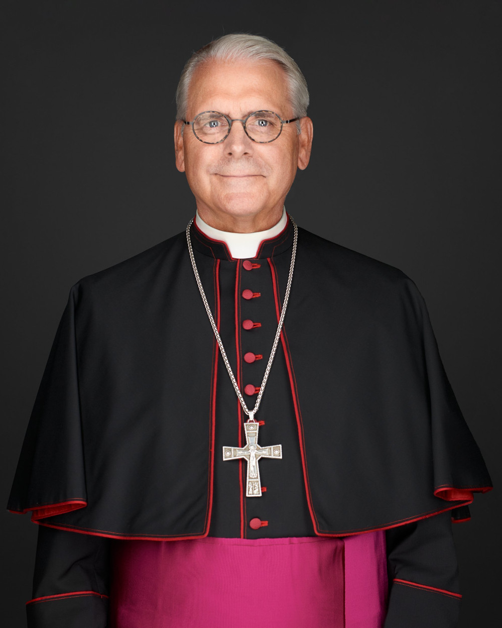 An older white man wears glasses, a bishop's cassock and a pectoral cross