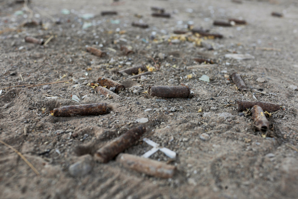 Rusted bullet casings lay in with sticks, other pieces of metal and faint tire tracks