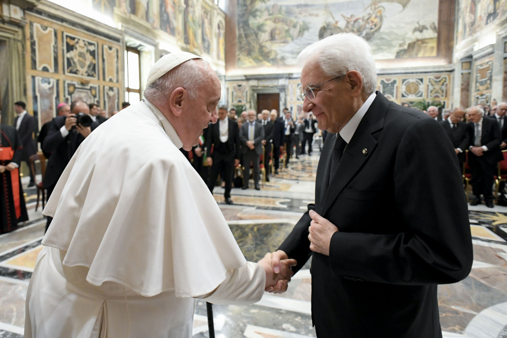 Pope Francis, using his cane, shakes the hand of an older white man wearing glasses