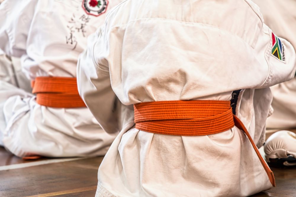 Closeup of person in white clothes tied with orange karate belt