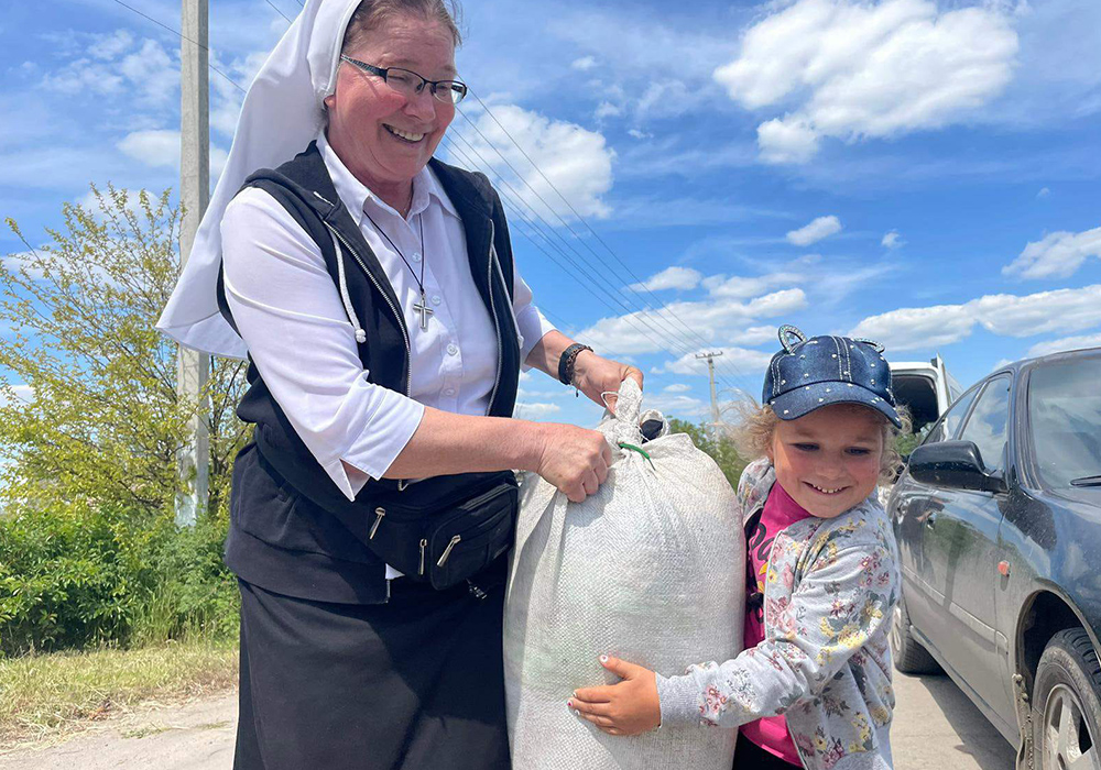 During a recent humanitarian mission to war-torn eastern Ukraine, a child assists Sr. Lydia Timkova carry a bag of supplies, in a village near Mykolaiv. Timkova has traveled across Ukraine to shepherd food and medical supplies to civilians living near the Russian front. (Courtesy of Lydia Timkova)