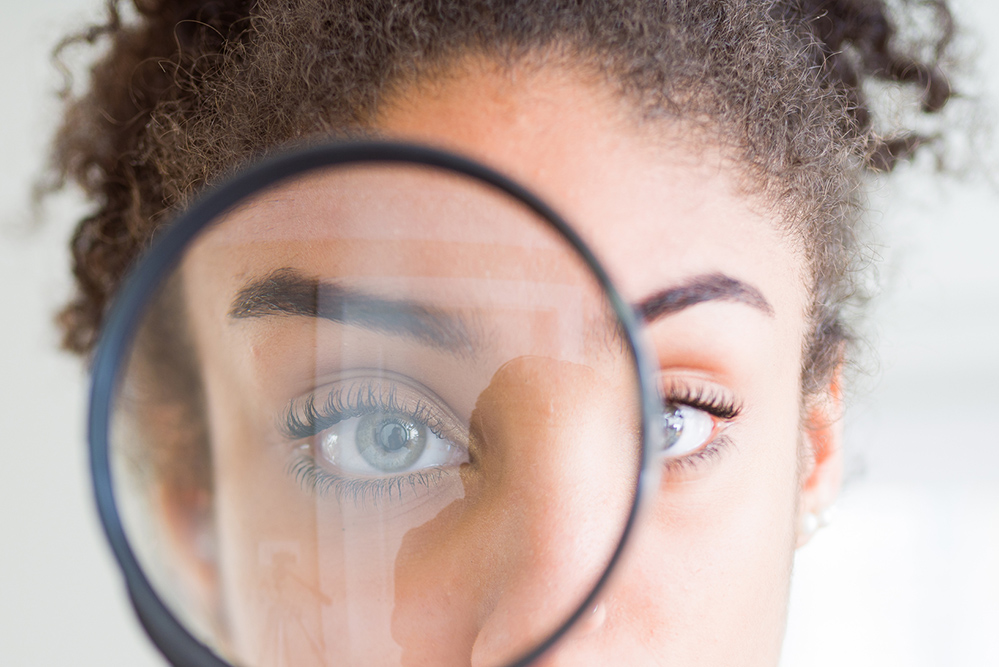 A woman looks through the lens of a magnifying glass (Dreamstime/Aaron Amat)