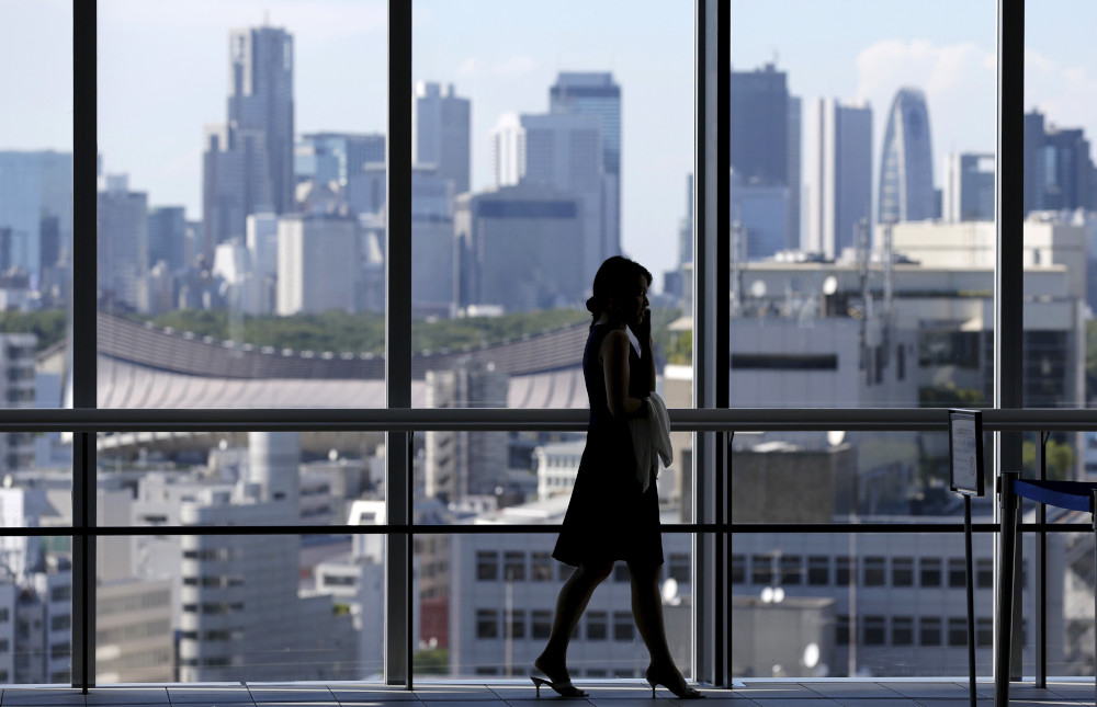 The silhouette of a woman talking into a cellphone is visible in front of large glass office building windows with more buildings outside the windows