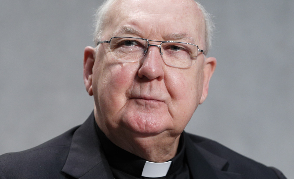 An older white man wearing glasses and a clerical collar looks at the camera