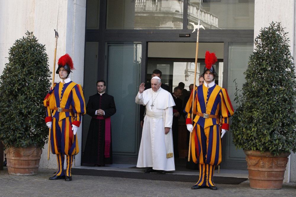 Pope Francis walks out of glass doors between members of the Swiss Guard