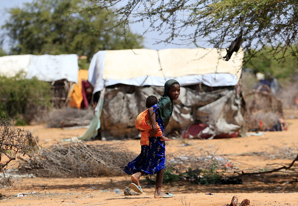 A young Somali refugee fleeing drought carries her sibling as they walk in the new arrivals area of the Hagadera refugee camp in Dadaab, near the Kenya-Somalia border, in Garissa County, Kenya, Jan. 17. (OSV News/Reuters/Thomas Mukoya)