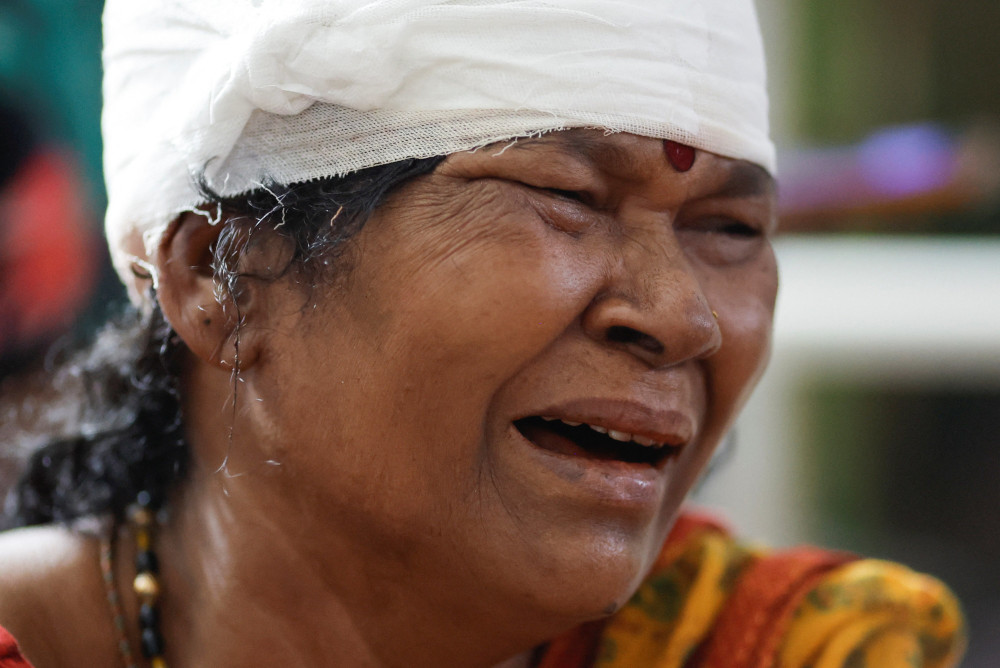 A woman wearing a bindi with a bandage wrapped around her head sobs