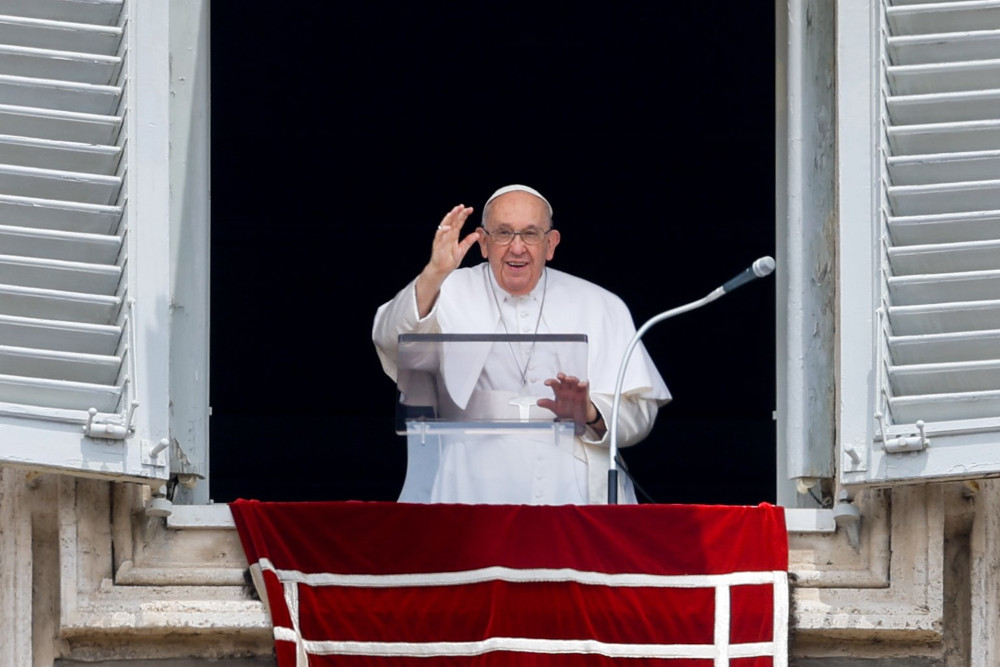 Pope Francis smiles and waves as he stands in the open window of his apartment