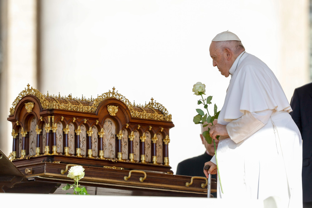 Pope Francis carries a white rose towards an ornate gold and wooden box