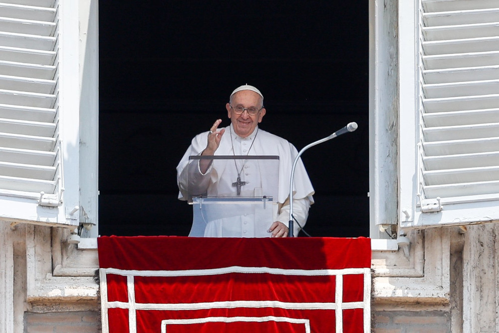 Pope Francis raises his hand as he stands in the window of his Vatican apartment