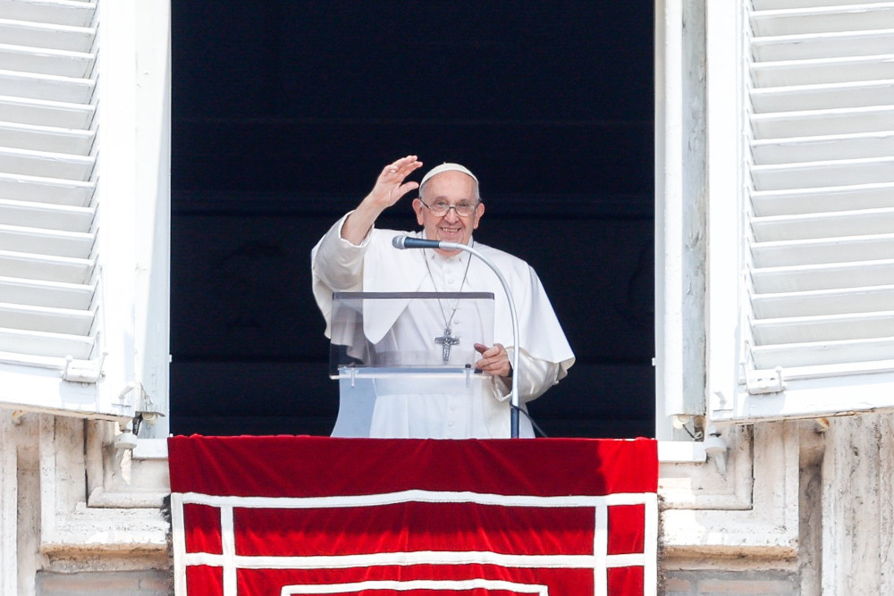Pope Francis raises his hand as he speaks from a clear podium at his window