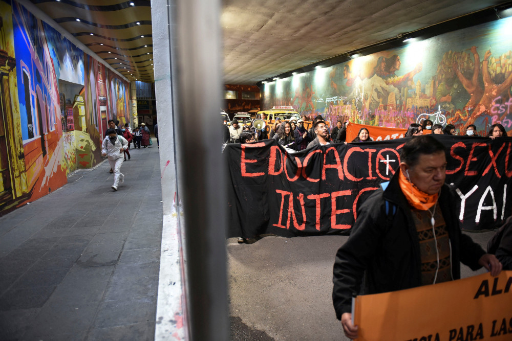 Bolivian people march under a roofed passage holding large black and orange banners