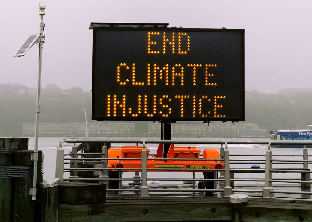 SIgn on highway reads: End climate injustice.