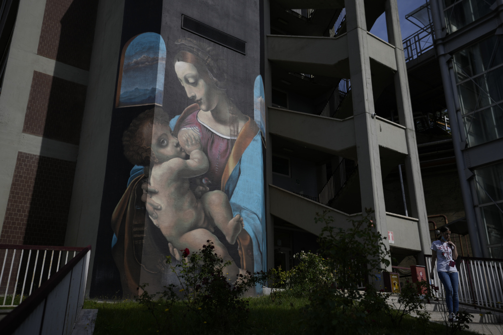A large banner painting of a white woman breastfeeding a white baby hangs on the side of a building
