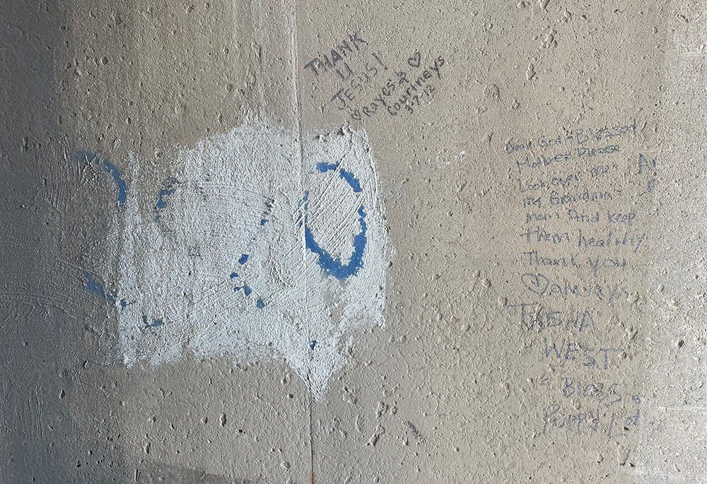 In this 2023 photo, taken to the right of the image known as Our Lady of the Underpass, someone had tagged a message in gray marker on the wall. "Dear God [and] Blessed Mother please look over my Grandma and Mom and keep them healthy thank you." (Gustavo Arellano)
