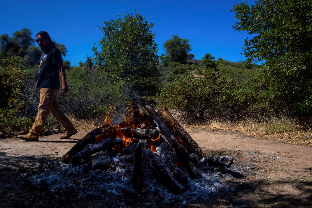 Morgun Frejo checks on rocks being heated in a fire for a sweat lodge on Oak Flat Campground, a sacred site for Native Americans located 70 miles east of Phoenix, on June 3, 2023, in Miami, Ariz. (AP Photo/Ty O'Neil)